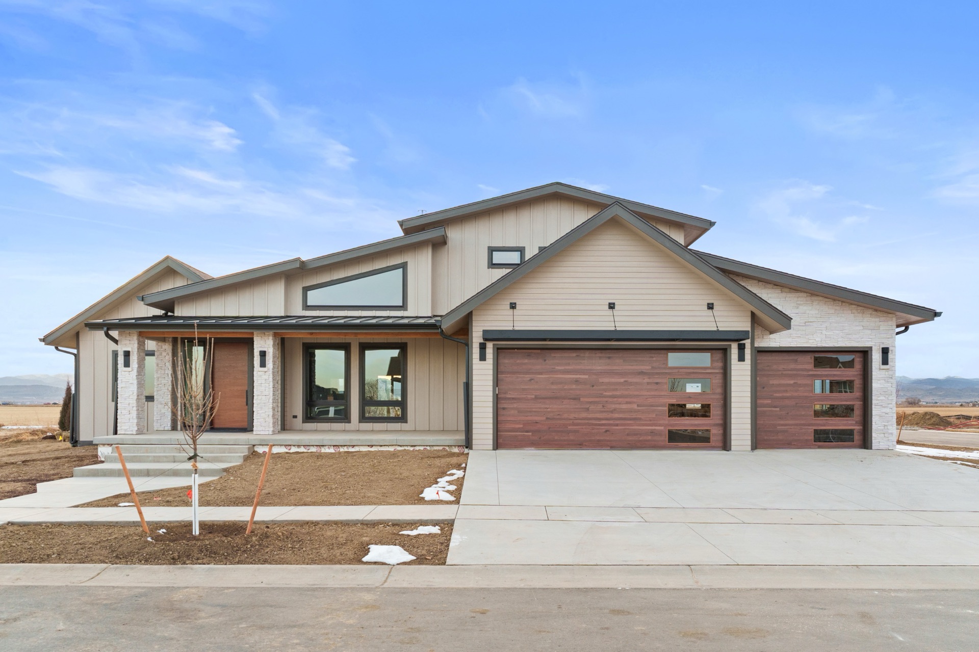 Modern craftsman front elevation with covered porch, stone columns, and wood-clad garage doors